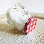Overturned mason jar with red lid spilling salt on a wooden surface, creating a rustic kitchen scene.