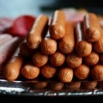 Delicious assortment of hot dogs and sliced meats artfully arranged on a silver platter.